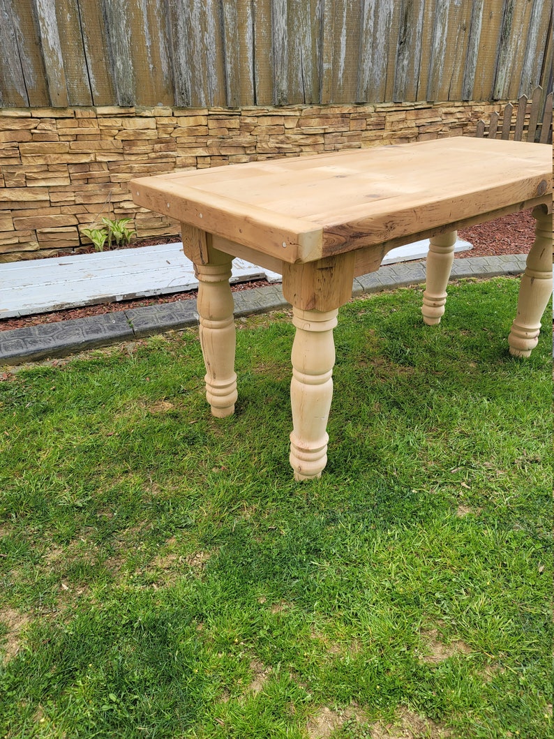 Puede incluir: Una mesa de madera r&uacute;stica con un acabado de madera natural y patas torneadas. La mesa est&aacute; sentada en un c&eacute;sped.
