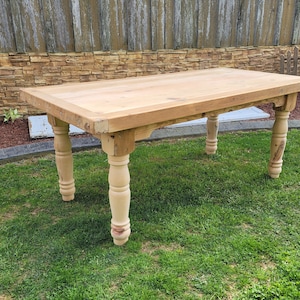 May include: A rustic wooden table with a natural wood finish and turned legs. The table is made of solid wood and has a rectangular top.