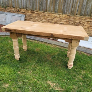 Puede incluir: Una mesa de madera clara con una tapa rectangular y patas torneadas. La mesa est&aacute; sentada en un c&eacute;sped.