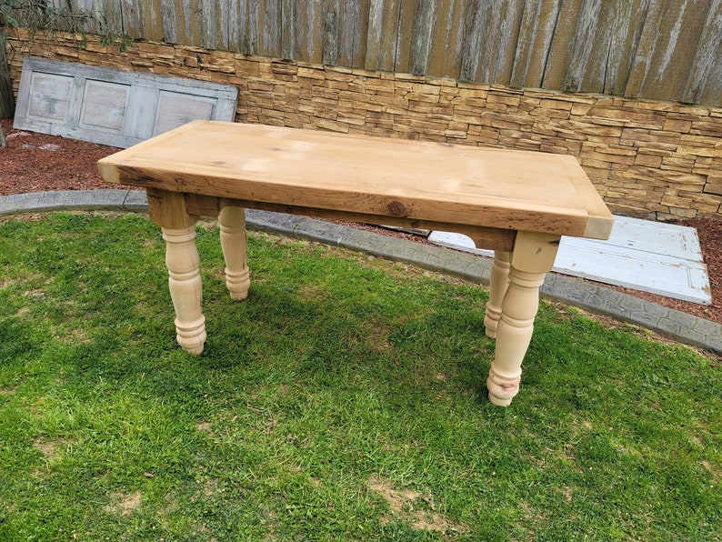 Puede incluir: Una mesa de madera clara con una tapa rectangular y patas torneadas. La mesa est&aacute; sentada en un c&eacute;sped.