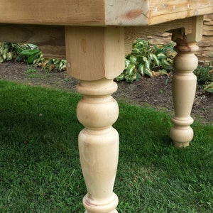 Puede incluir: Una mesa de madera con un acabado natural y patas torneadas. La mesa est&aacute; sentada en un c&eacute;sped.