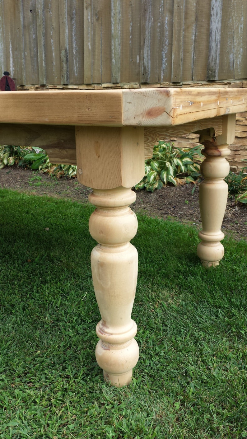 Puede incluir: Una mesa de madera con un acabado natural y patas torneadas. La mesa est&aacute; sentada en un c&eacute;sped.