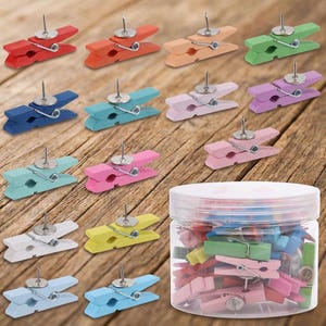 May include: A collection of multi-colored wooden clothespins, each featuring a silver metal push pin attached to the top. The set includes various shades such as red, orange, green, blue, pink, and white, stored in a clear plastic jar.