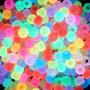 Könnte beinhalten: Eine Ansammlung kleiner, runder, durchscheinender Kunststoffperlen in einer Vielzahl leuchtender Neonfarben wie Pink, Orange, Gelb, Grün und Blau. Jede Perle hat eine glatte, matte Oberfläche und ein mittiges Loch zum Auffädeln.