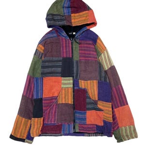 Può includere: Una giacca con cappuccio e cerniera caratterizzata da un design patchwork composto da vari pannelli di tessuto rettangolari nei toni dell'arancione, viola, verde e nero. Il capo include una chiusura frontale con zip, un cappuccio e due tasche.