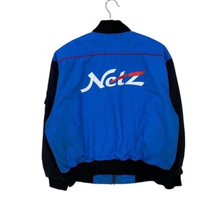 May include: A blue and black bomber jacket featuring the word Netz printed in white with a red accent line across the back. The jacket has a high collar, long sleeves with black panels, and a ribbed black hem at the waist and cuffs.