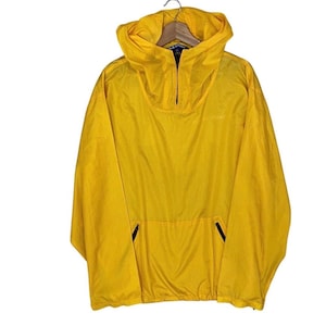 May include: A bright yellow pullover windbreaker jacket featuring a hood, a partial front zip closure, long sleeves, and a large front kangaroo pocket with black zip accents. The fabric has a subtle grid pattern texture throughout the garment.