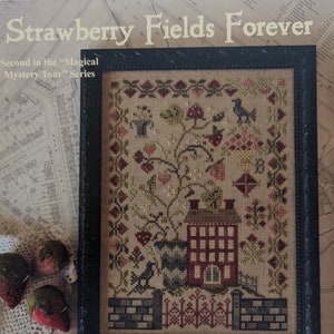 May include: Framed cross-stitch sampler titled "Strawberry Fields Forever" with a black frame. The design features a red brick building, birds, and floral elements. The text "Blackbird Designs" is at the bottom.