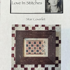 May include: A framed needlepoint piece titled "Star Coverlet" with a brown wooden frame. The needlepoint features a pattern of blue and red stars. The image includes text that reads "Lucy Beam Love In Stitches" and "Designed by Rebecca Noland".