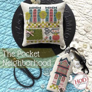May include: A cross stitch pattern for a small pillow featuring a neighborhood with houses, trees, and a cat. The text "The Pocket Neighborhood" is written below the pillow.