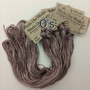 Könnte beinhalten: Ein Bündel mit sechs Knäuelen Stickgarn von Weeks Dye Works in der Farbe "Oyster" (1147). Das Garn ist meliert, mit Schattierungen von Lila und Beige. Die Knäuel sind mit dem Weeks Dye Works Logo und dem Farbnamen und der Nummer beschriftet.