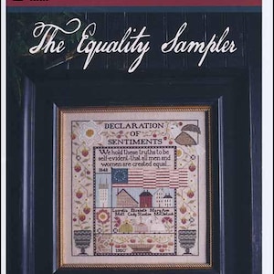 May include: A framed cross-stitch sampler titled "The Equality Sampler" by Plum Street Samplers. The sampler features a Declaration of Sentiments, an American flag, and various buildings. The text reads "We hold these truths to be self-evident that all men and women are created equal."