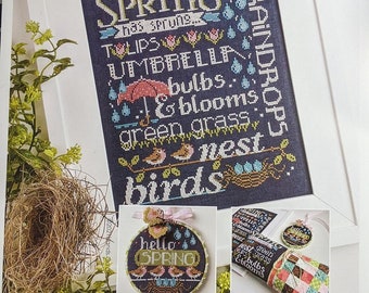May include: A cross-stitch pattern featuring a blue background with the words "Spring, Tulips, Umbrella, Bulbs, & Blooms, Green Grass, Nest, Birds" in colorful lettering. The pattern is framed with a white border. The image also includes two smaller cross-stitch patterns, one with the words "Hello Spring" and the other with the words "Rest, Green Grass, & Bulbs".