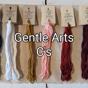 May include: Six spools of Gentle Arts embroidery floss in the colors black, white, gold, pink, red, and burgundy. The Gentle Arts logo is visible on each spool.