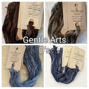 May include: A collection of Gentle Arts embroidery floss in various colors, including dark chocolate, deep forest, dungarees, and distressed denim. Each skein is labeled with its color name and number. The image also includes the text "Gentle Arts" and "D's".
