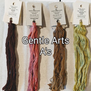 May include: Four spools of embroidery floss in different colors: brown, pink, brown, and green. The spools are labeled with the text "The Gentle Art" and the color names "Acorn", "Antique Rose", "Apple Cider", and "Avocado".