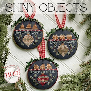 May include: Three round, blue, felt ornaments with white stitching and a red and white gingham ribbon. The ornaments feature a brown and gold ornament with a green wreath and the text "Peace on Earth", "Joy to the World", and "Happy Holidays".