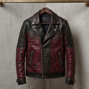 Puede incluir: Una chaqueta estilo motero con una textura de relieve de cocodrilo en dos tonos, negro y rojo oscuro. La chaqueta incluye solapas, una cremallera frontal asimétrica, varios bolsillos con cremallera y correas con hebilla en los puños.