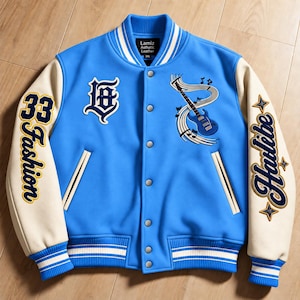 Op de afbeelding: Een felblauw varsity-jack met crèmekleurige mouwen, voorzien van een blauwe elektrische gitaar met muzieknoten, de letters LB en de tekst 33 Fashion en Hailibe geborduurd in marineblauw en geel op de mouwen en de borst.