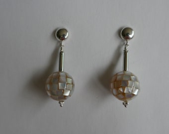 May include: A pair of silver earrings with a round, white and brown, geometric patterned bead on each earring.