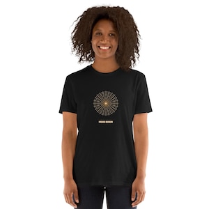 Peut inclure: Un t-shirt noir à manches courtes avec un motif de grille circulaire de couleur dorée centré sur la poitrine. Sous le motif circulaire, le texte HIGGS BOSON est imprimé dans une police sans empattement dorée assortie. Col rond.