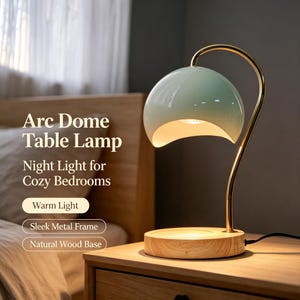 Op de afbeelding: Een tafellamp met een lichtgroene koepelvormige kap, een gebogen goudkleurige metalen arm en een ronde voet van natuurlijk hout. De tekst op de afbeelding luidt: Arc Dome Table Lamp, Night Light for Cozy Bedrooms, Warm Light, Sleek Metal Frame, Natural Wood Base.