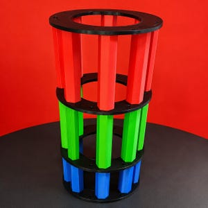 Peut inclure: Une structure cylindrique composée de trois anneaux circulaires noirs empilés et reliés par des piliers hexagonaux verticaux. La section supérieure présente des piliers rouges, la section centrale des piliers verts et la base des piliers bleus.