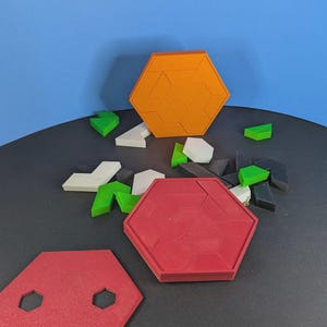 May include: A set of hexagonal puzzle frames and assorted geometric pieces in orange, red, white, green, and black. The collection includes two assembled hexagonal frames, one red flat hexagonal plate with two small cutouts, and loose pieces.