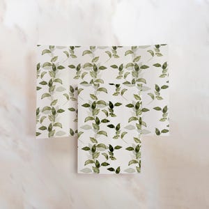 May include: Two sheets of white wrapping paper with a green leaf pattern. The paper is folded in half and the pattern is visible on both sides.