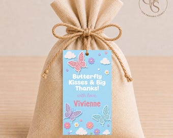 Op de afbeelding: Een beige stoffen buidel met een jute trekkoord, voorzien van een rechthoekig lichtblauw label. Het label toont roze en blauwe vlinders, witte wolken, kleine bloemen en de tekst: Butterfly Kisses & Big Thanks! with love, Vivienne.