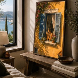 May include: A framed rectangular wall art print depicting a sunlit yellow Mediterranean building facade with open blue shutters, a person holding a cup at the window, and flowering vines, resting on a wooden bench next to two stacked books.