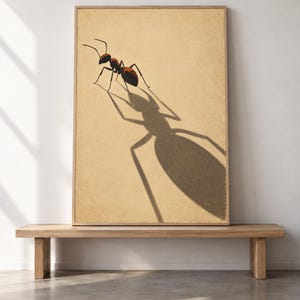 May include: A rectangular framed wall art print featuring a detailed illustration of a single ant on a textured beige background. The ant is rendered in shades of brown and black, casting a long, dramatic, and oversized shadow across the surface.
