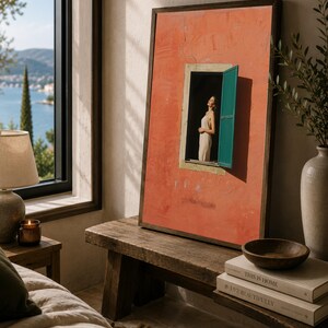 Op de afbeelding: Een ingelijst rechthoekig wandkunstwerk met een getextureerde muur in terracotta-kleur en een enkel open raam. Een persoon in een lichtgekleurde jurk staat in het raamkozijn, dat is voorzien van een helderblauwgroene luik. Donkerhouten lijst.