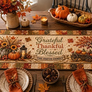 May include: A rectangular quilted table runner featuring a patchwork border in autumn colors and a central panel with the text "Grateful Thankful Blessed" and "THE SMITH FAMILY". The design includes sunflowers, pumpkins, a lantern, and a wagon.
