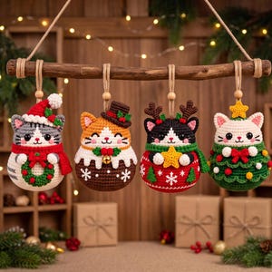 May include: Four crocheted cat ornaments hanging from a wooden branch. The first cat wears a Santa hat and scarf with a wreath. The second wears a top hat and brown jumper. The third has reindeer antlers and a red jumper. The fourth wears a tree costume.