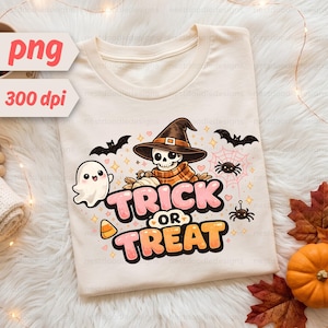 May include: A cream-coloured t-shirt featuring a graphic of a skeleton wearing a witch hat, a small ghost, bats, spiders, and a spiderweb. The text "TRICK OR TREAT" is printed in large, bold pink and orange letters below the central illustration.