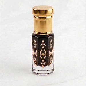 May include: A small, hexagonal glass perfume bottle labeled OUD JUNAID, featuring a dark liquid interior and a gold-colored metallic cap. The exterior glass is decorated with a repeating gold-toned geometric pattern of diamonds and star shapes.