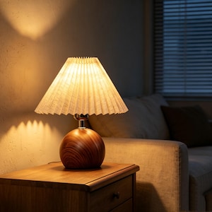 May include: A table lamp featuring a spherical wooden base with a visible grain pattern and a pleated, cone-shaped lampshade. The lamp emits a warm, soft glow, illuminating the surrounding area with a focused light pattern.