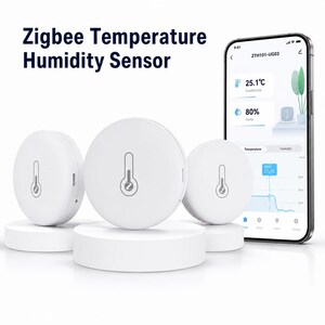 Op de afbeelding: Drie witte ronde Zigbee temperatuur- en vochtigheidssensoren met een thermometerpictogram op de voorzijde. Een smartphone toont de ZTH101-UG03 app-interface met 25,1 graden Celsius en 80 procent luchtvochtigheid met een grafiek.