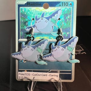 May include: A pair of dangle earrings featuring a light blue and purple Mantine character with a small green Remoraid attached. The earrings are displayed on a Mantine Pokemon trading card with the text PokeTCG - CutOut Card - Earring.