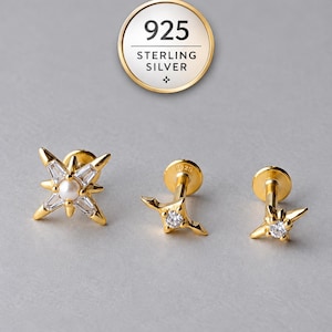 Può includere: Tre orecchini a lobo dorati con motivi a stella. Uno presenta una perla centrale con pietre taglio baguette, mentre due più piccoli hanno singole pietre rotonde. Un badge circolare riporta la scritta 925 STERLING SILVER.
