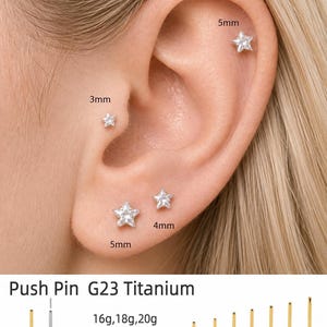 Puede incluir: Un conjunto de pendientes push pin de titanio G23 con gemas transparentes en forma de estrella de 3mm, 4mm y 5mm. El producto incluye postes de base plana en calibres 16g, 18g y 20g con longitudes de 5mm a 12mm, en tonos oro y plata.