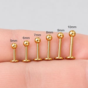 May include: Six gold-colored metal labret studs with ball ends, arranged in a row by length. The posts are labeled with their respective lengths of 5mm, 6mm, 7mm, 8mm, 9mm, and 10mm, indicating the specific size of each individual piece of jewelry.