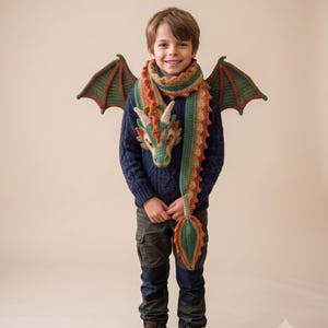 Può includere: Una sciarpa a forma di drago realizzata all'uncinetto, con una testa di drago dettagliata, un corpo lungo con una cresta spinosa e due grandi ali verdi e marroni. La sciarpa è realizzata in tonalità verde bosco, crema e arancione bruciato.