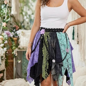 Puede incluir: Una camiseta sin mangas blanca combinada con una falda de varias capas con paneles de encaje y tela en morado, negro, verde oliva y verde menta. La falda tiene una cintura de encaje negro, un pequeño adorno de flor morada y una mariposa.