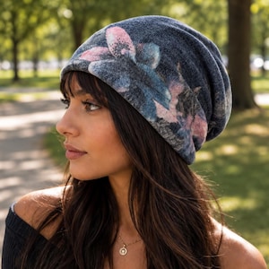 May include: A slouchy beanie hat in a dark charcoal gray fabric featuring a prominent floral pattern in shades of muted pink and blue. The knit material has a soft, heathered texture, and the hat is designed with a relaxed, loose-fitting silhouette.