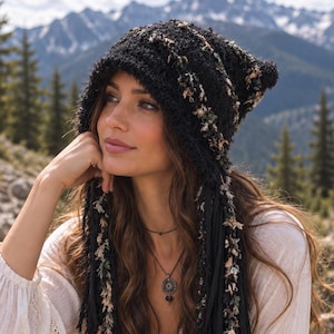 Puede incluir: Una capucha de punto negro con largos flecos colgantes en tonos negro, beige y verde apagado. Esta pieza texturizada está confeccionada con una combinación de hilo negro sólido y tiras de tela deshilachadas de colores variados que cuelgan.