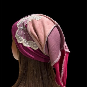 May include: A colorful head covering in shades of pink and purple, with a butterfly design. The head covering is made of soft fabric and has a knotted end. The head covering is designed to be worn on the head.