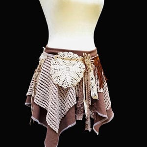 May include: A brown and cream-colored bohemian skirt with a layered design. The skirt features crochet, lace, and fabric details, with a large cream-colored doily accent at the waist. The skirt is displayed on a mannequin.