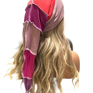 May include: A patchwork head covering featuring a ribbed mauve band and a long, pointed tail constructed from multiple fabric panels in shades of bright red, deep magenta, muted brown, and dark purple, all joined with visible light-colored stitching.